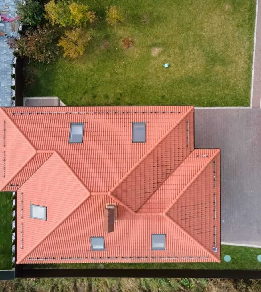 Aerial view of a house with a red tiled roof and surrounding green yard.