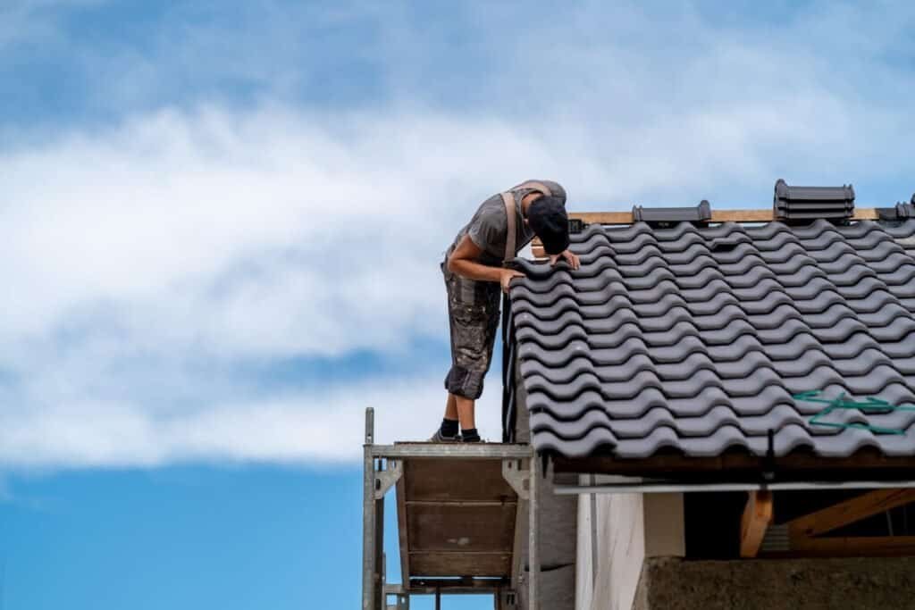 Roofing professional inspecting roof tiles on residential building.